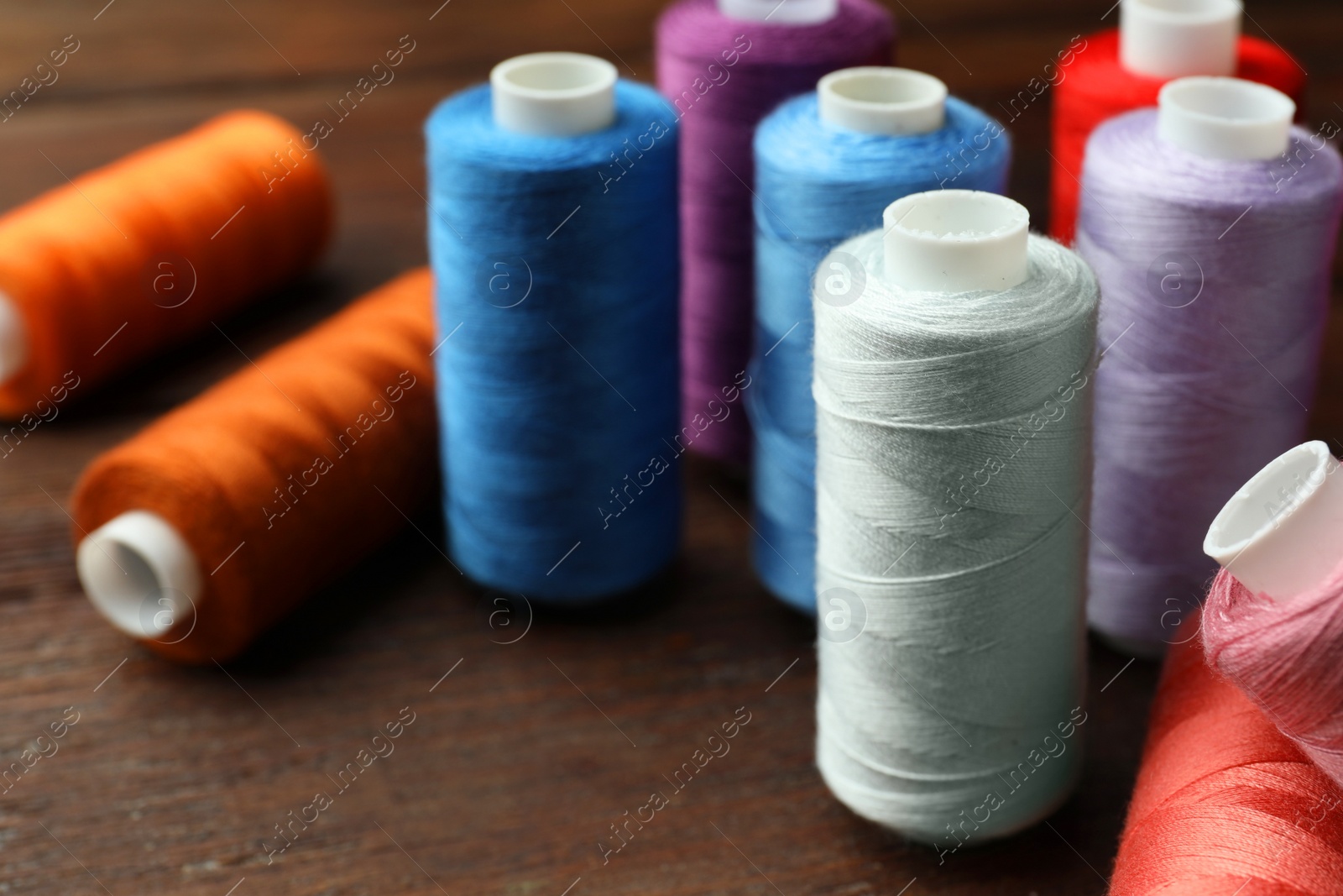 Photo of Different colorful sewing threads on wooden table, closeup