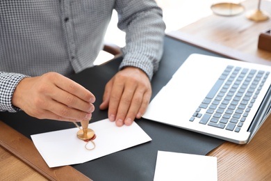 Photo of Male notary stamping document at table in office, closeup