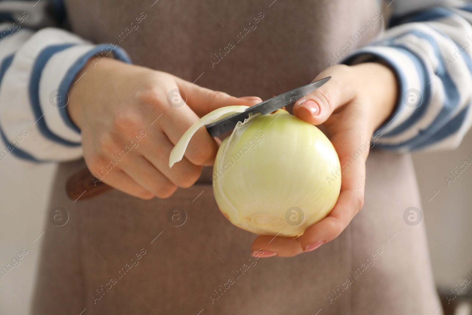 Photo of Woman peeling fresh onion with knife indoors, closeup