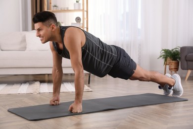 Photo of Handsome man doing plank exercise on yoga mat at home