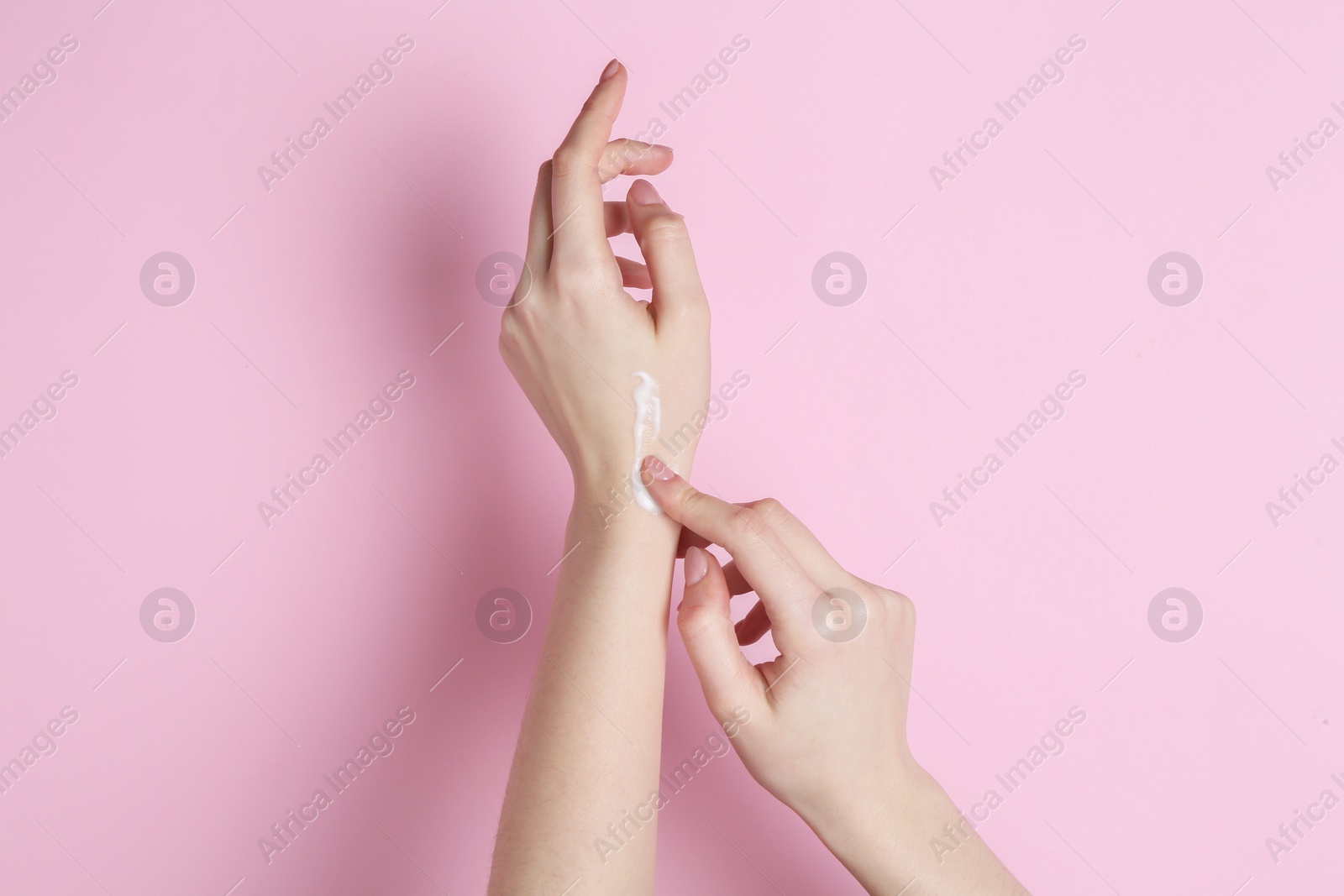 Photo of Woman applying cream on her hand against pink background, closeup