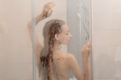 Young woman taking shower, view through glass door