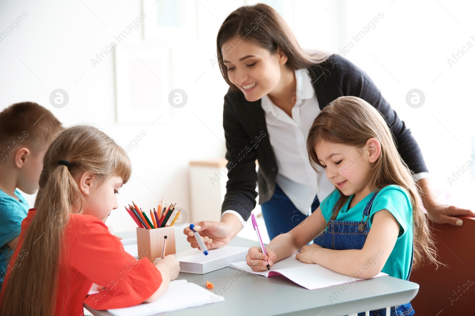 Photo of Female teacher helping girl with her task in classroom at school