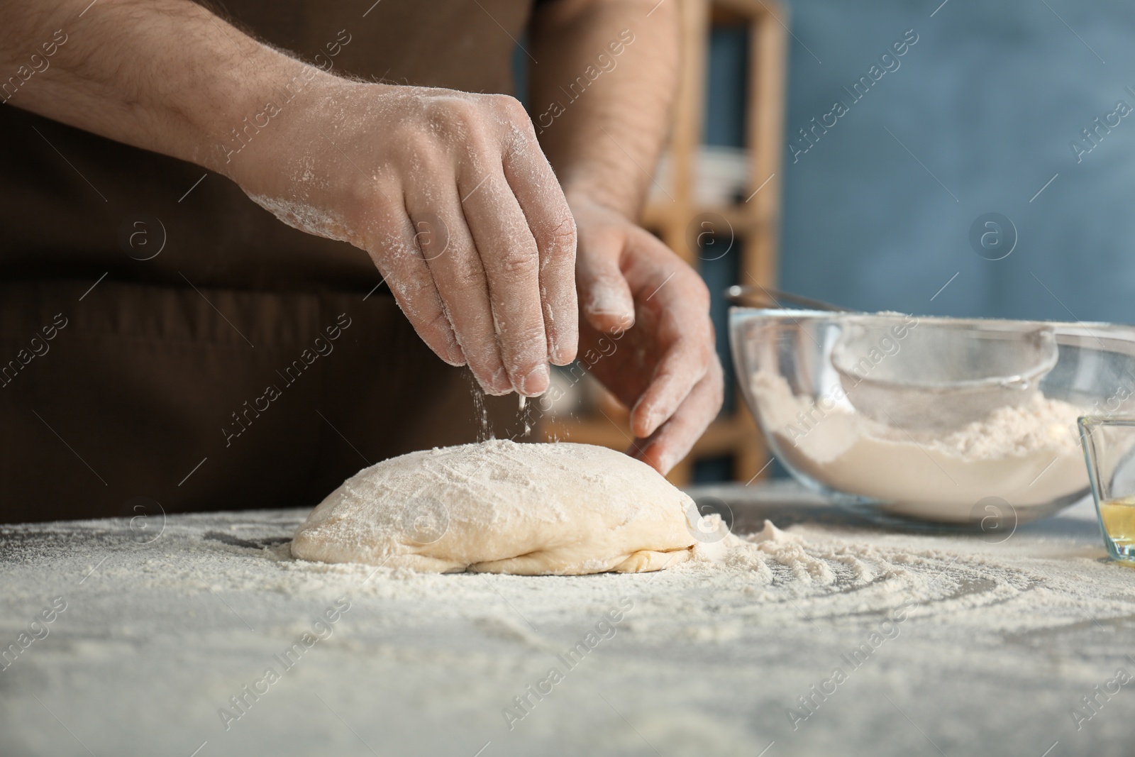 Photo of Man sprinkling flour over dough on table in kitchen