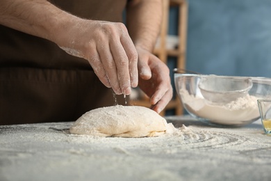 Man sprinkling flour over dough on table in kitchen