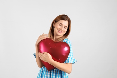 Portrait of woman with heart shaped balloon on light background