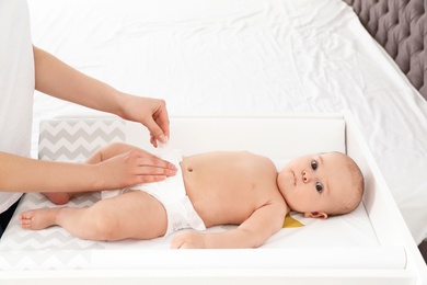 Mother changing her baby's diaper on table indoors