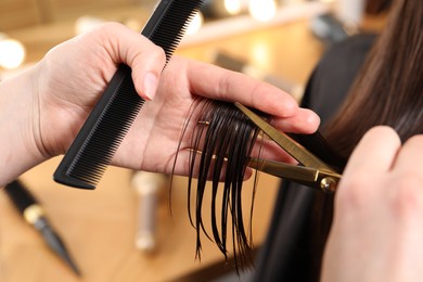 Hairdresser cutting client's hair with scissors in salon, closeup