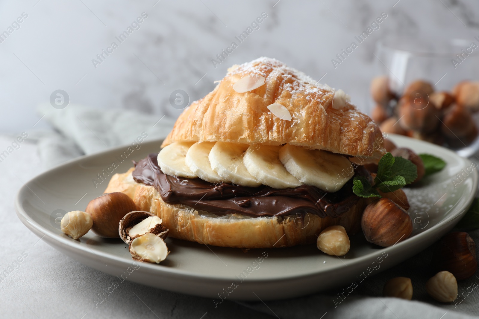 Photo of Delicious croissant with banana, chocolate and hazelnuts on gray table, closeup