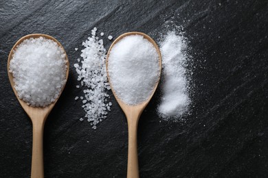 Photo of Organic salt in spoons on black table, flat lay. Space for text