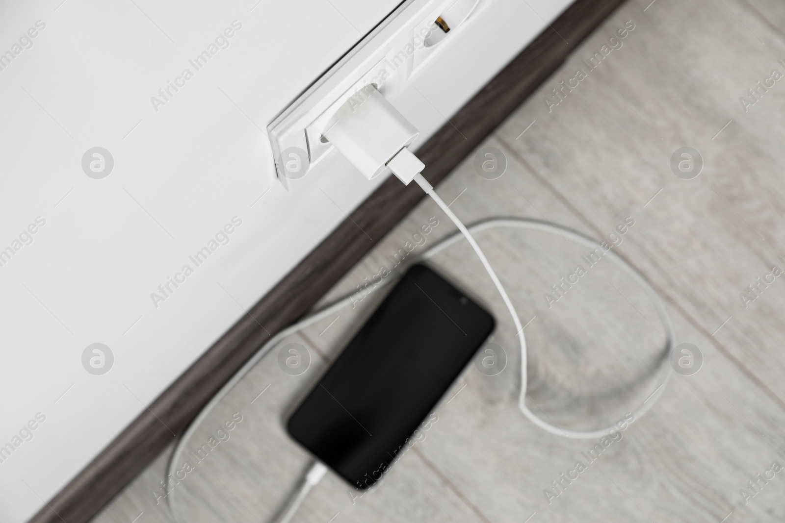 Photo of Modern smartphone charging from electric socket indoors, above view