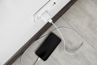 Photo of Modern smartphone charging from electric socket indoors, above view