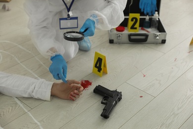 Photo of Investigator in protective suit working at crime scene with dead body, closeup