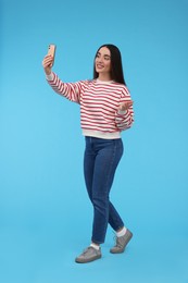 Photo of Smiling young woman taking selfie with smartphone on light blue background