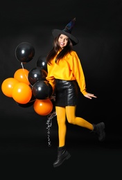 Photo of Beautiful woman wearing witch costume for Halloween party jumping with balloons on black background