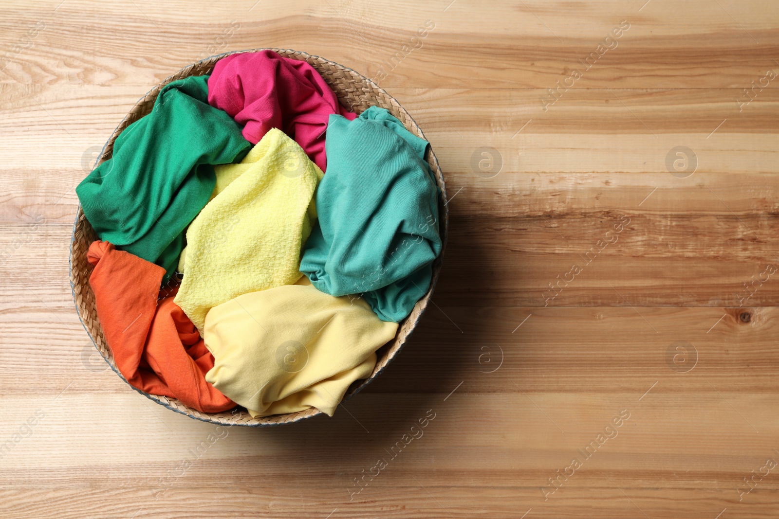 Photo of Wicker basket with laundry on wooden surface, top view. Space for text