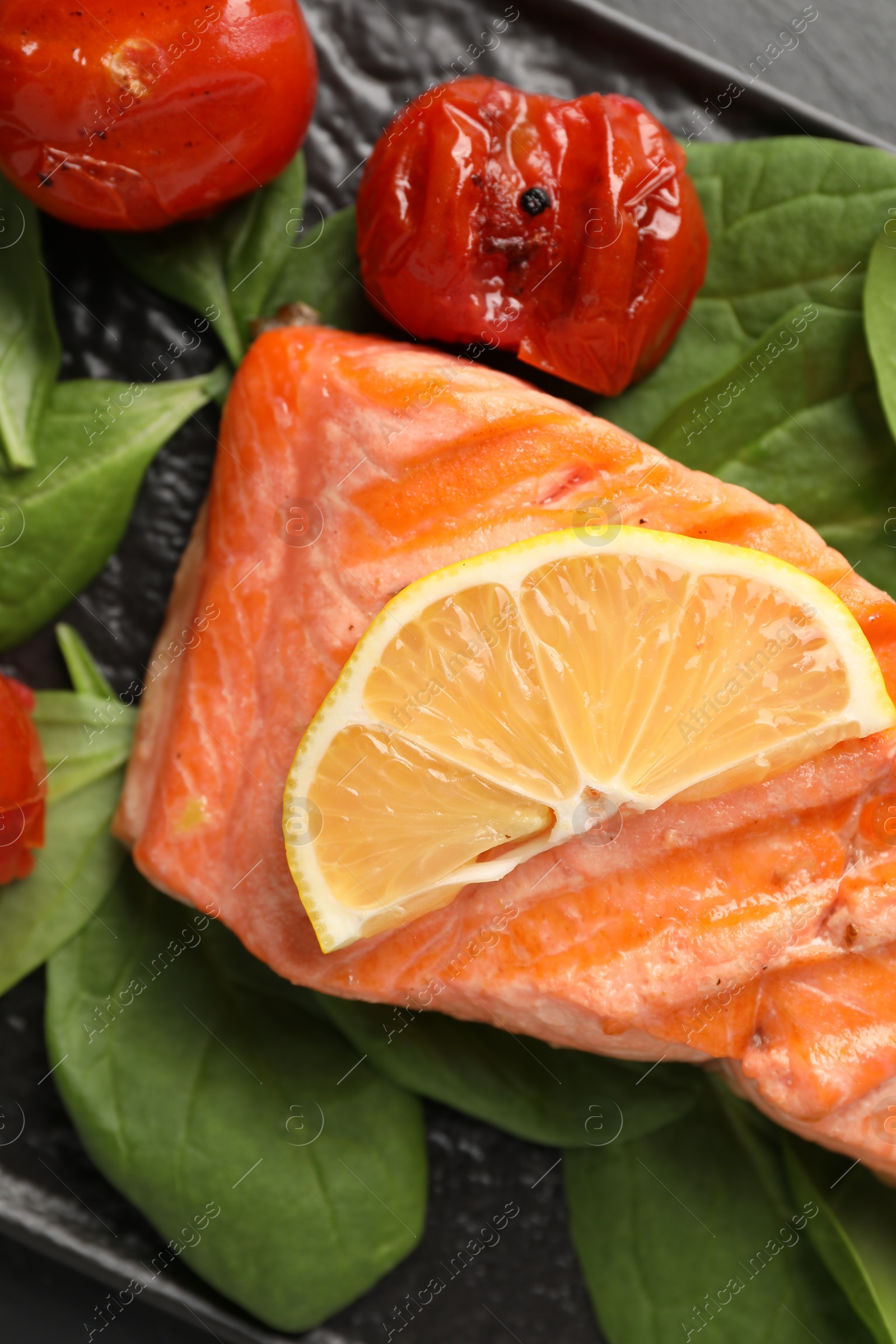 Photo of Tasty grilled salmon with tomatoes, spinach and lemon on table, top view