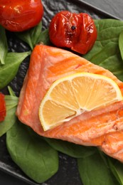 Photo of Tasty grilled salmon with tomatoes, spinach and lemon on table, top view