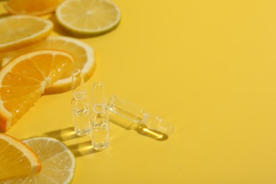 Photo of Skincare ampoules with vitamin C and citrus slices on yellow background, closeup. Space for text
