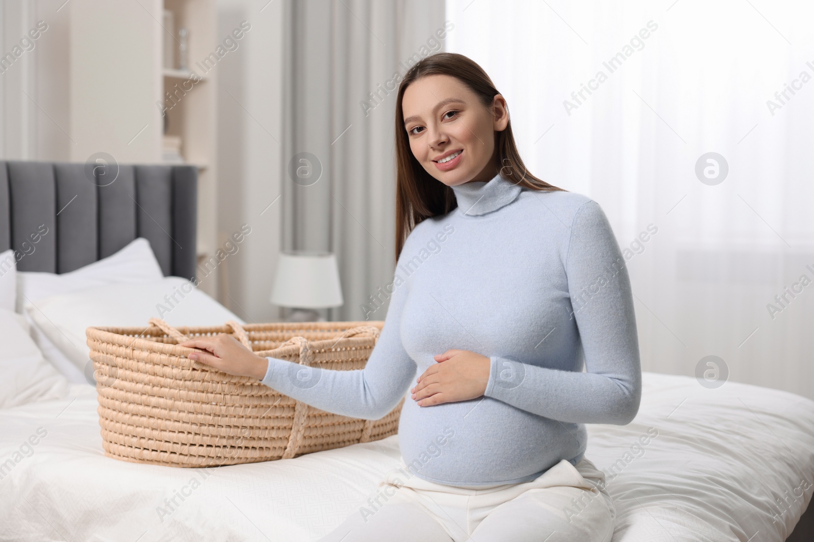 Photo of Beautiful pregnant woman with baby basket in bedroom