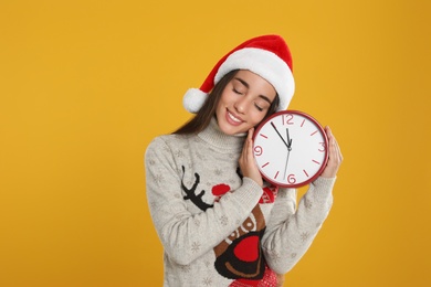 Photo of Woman in Santa hat with clock on yellow background. Christmas countdown
