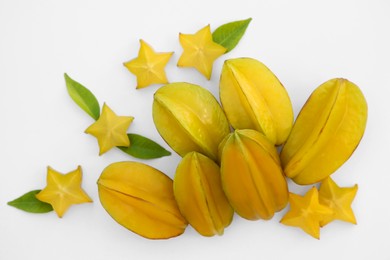 Photo of Delicious cut and whole carambolas, green leaves on white background, top view