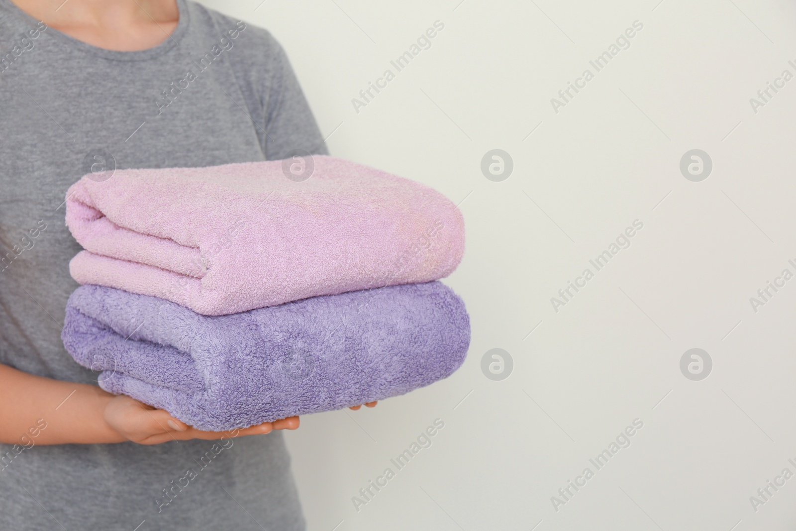 Photo of Woman holding folded soft terry towels on light background, closeup. Space for text