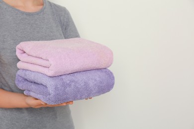 Photo of Woman holding folded soft terry towels on light background, closeup. Space for text