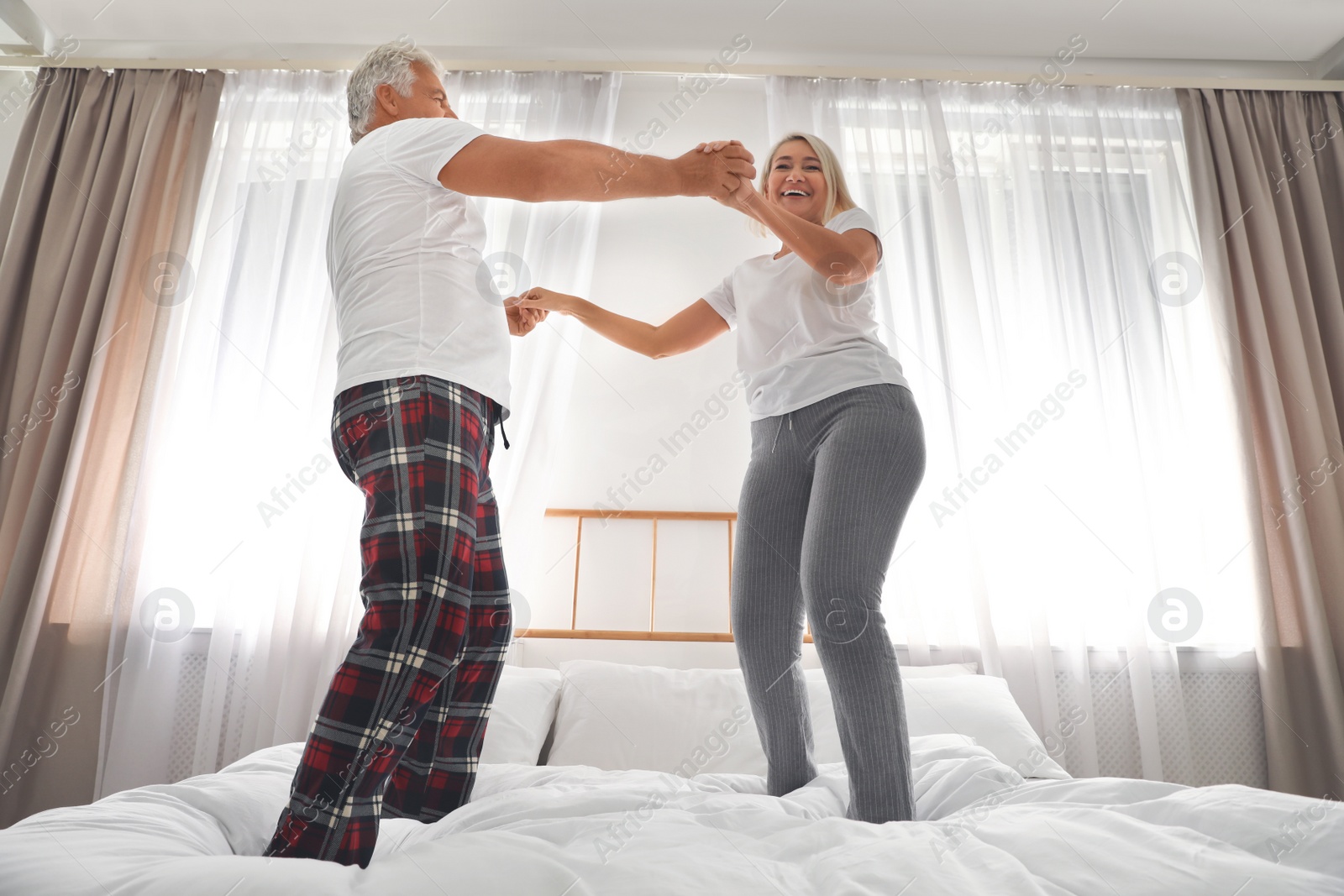 Photo of Happy mature couple dancing together on bed at home, low angle view
