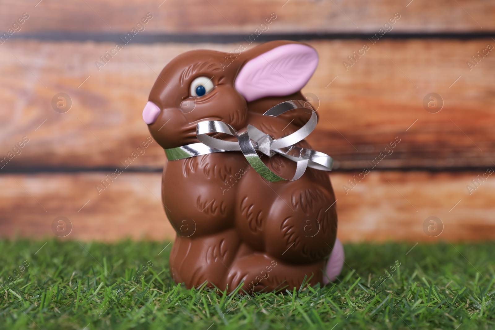 Photo of Easter celebration. Cute chocolate bunny on grass against wooden background