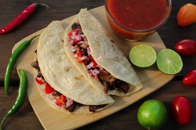 Delicious tacos with meat, vegetables and sauce on wooden table, above view