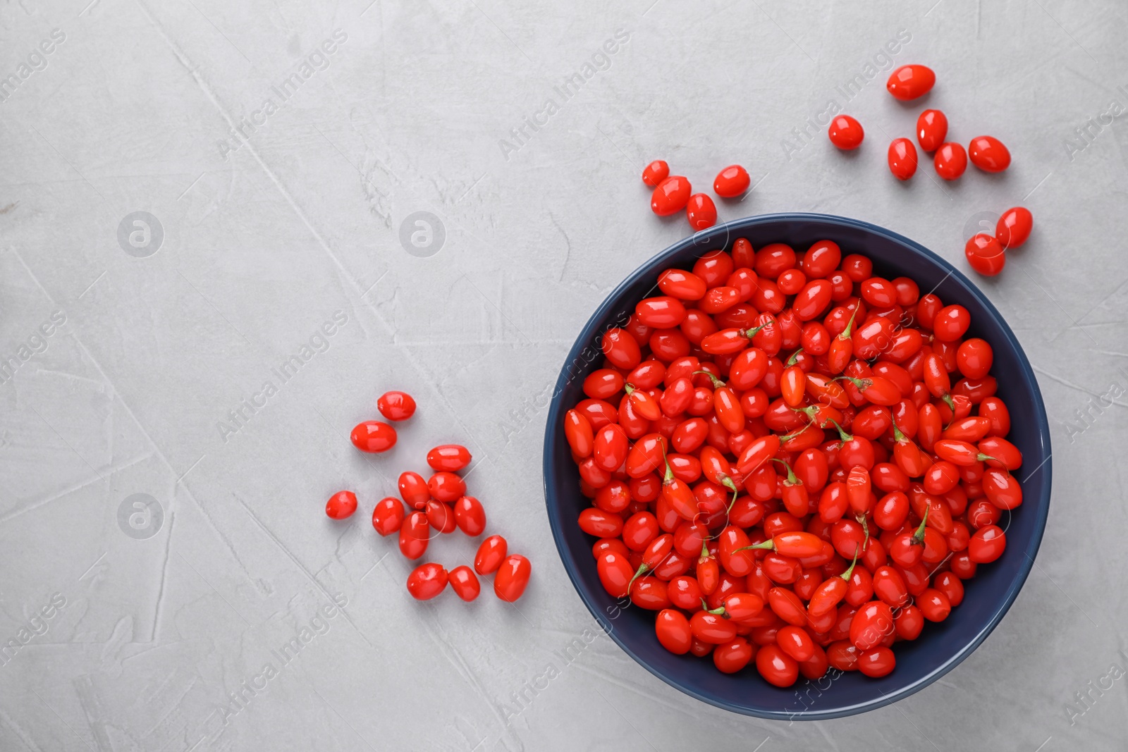 Photo of Bowl with fresh goji berries on grey background, flat lay. Space for text