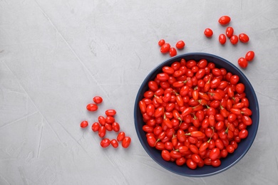 Bowl with fresh goji berries on grey background, flat lay. Space for text