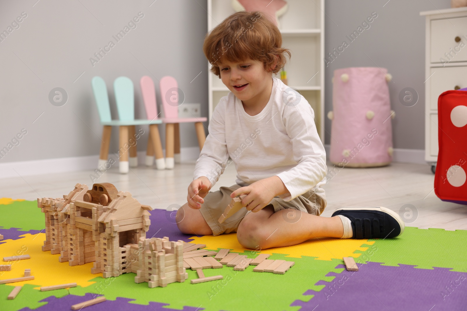 Photo of Little boy playing with wooden construction set on puzzle mat in room. Child's toy