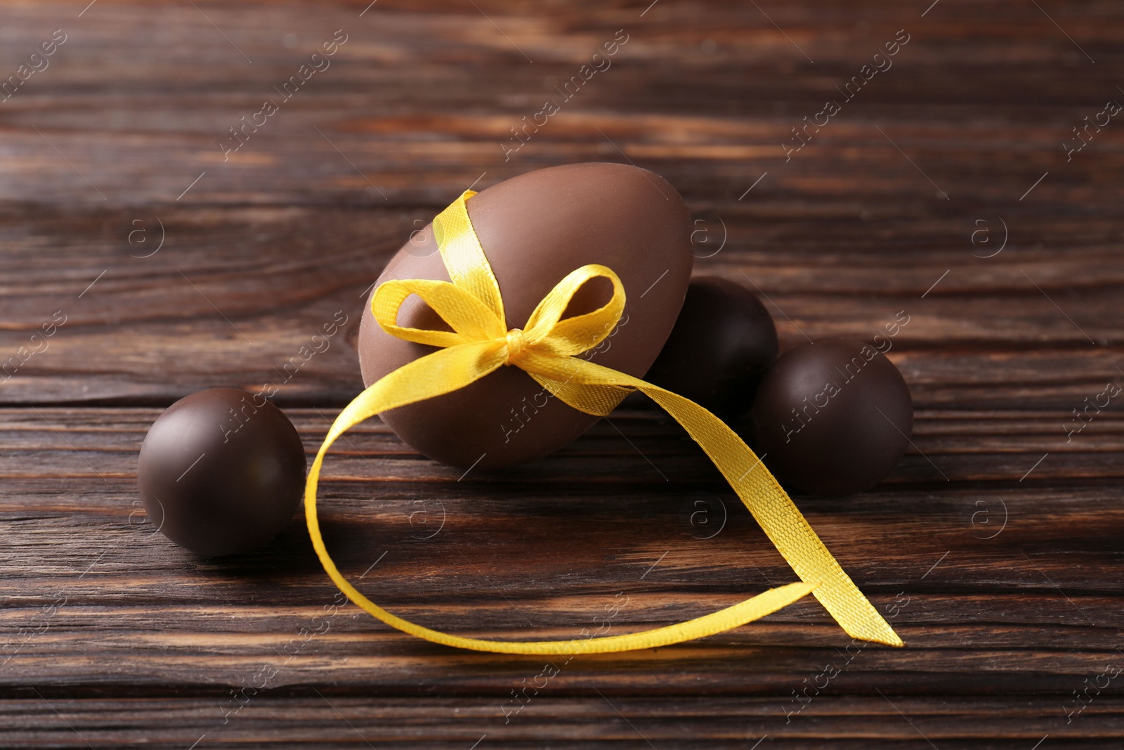 Photo of Tasty chocolate egg with yellow bow and sweets on wooden table