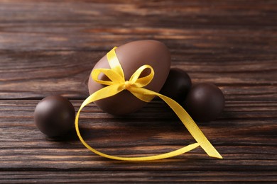 Photo of Tasty chocolate egg with yellow bow and sweets on wooden table