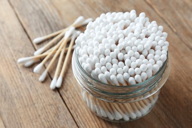 Photo of Many cotton buds and glass jar on wooden table
