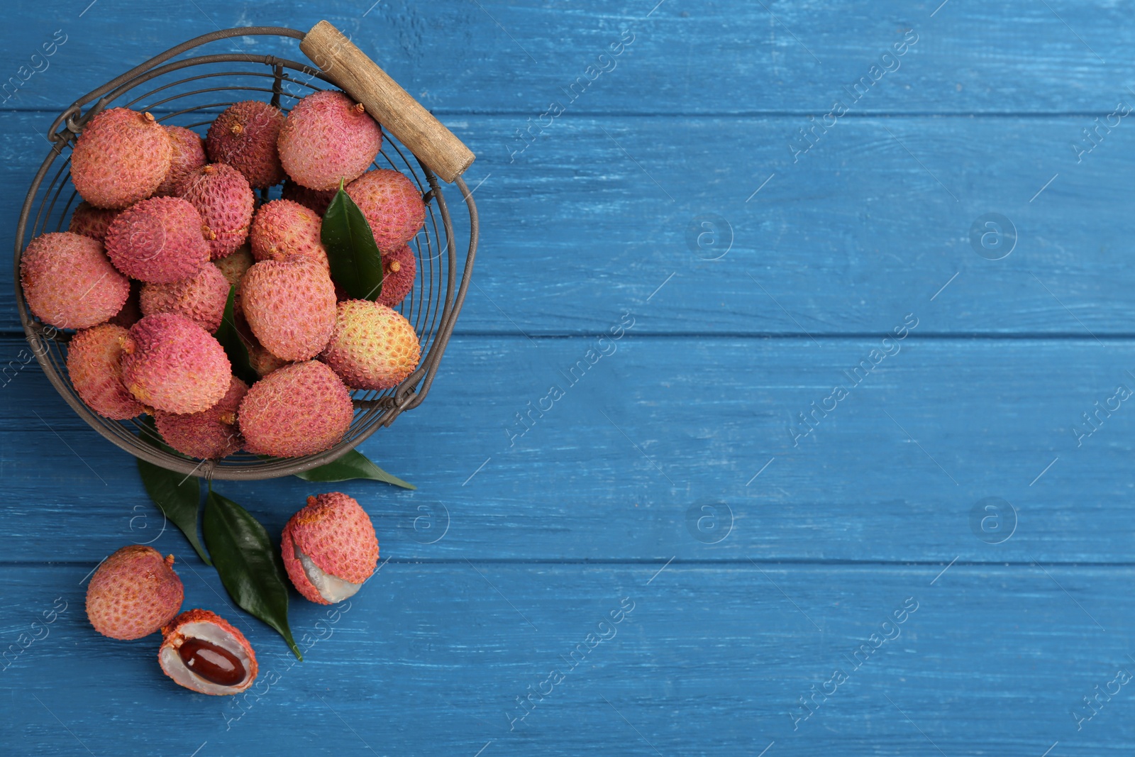 Photo of Fresh ripe lychee fruits in metal basket on blue wooden table, flat lay. Space for text