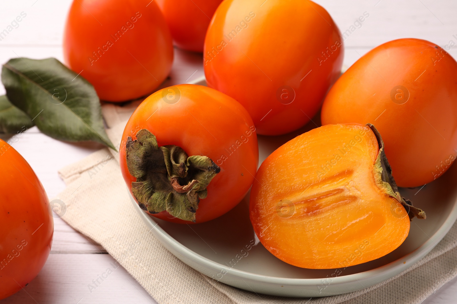 Photo of Delicious ripe juicy persimmons on white wooden table, closeup