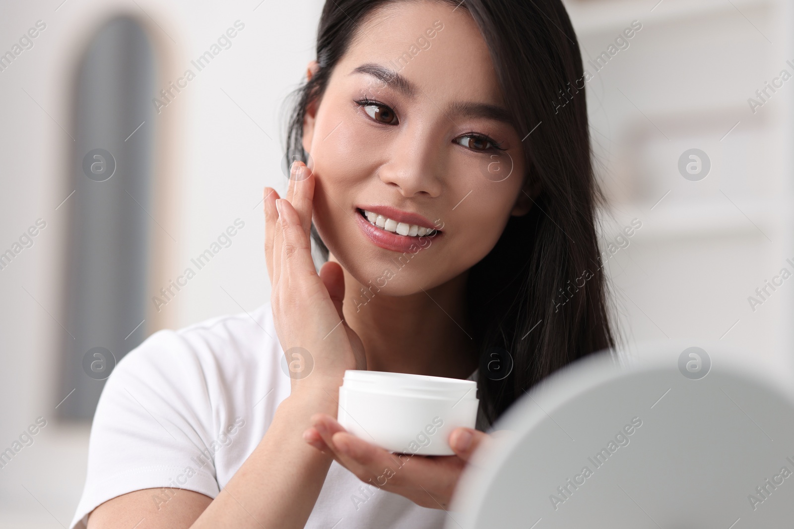 Photo of Happy woman applying face cream at home