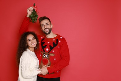 Photo of Portrait of lovely couple under mistletoe bunch on red background. Space for text