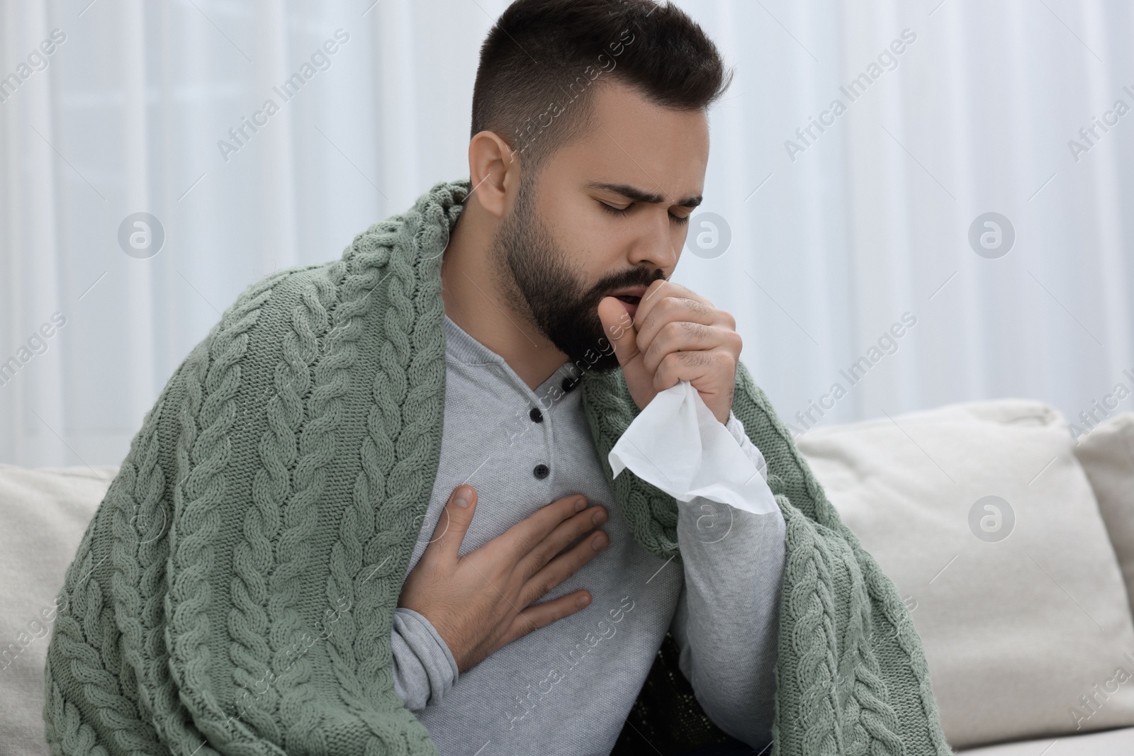 Photo of Sick man with tissue coughing at home