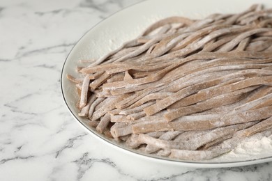 Photo of Uncooked homemade soba (buckwheat noodles) on white marble table, closeup