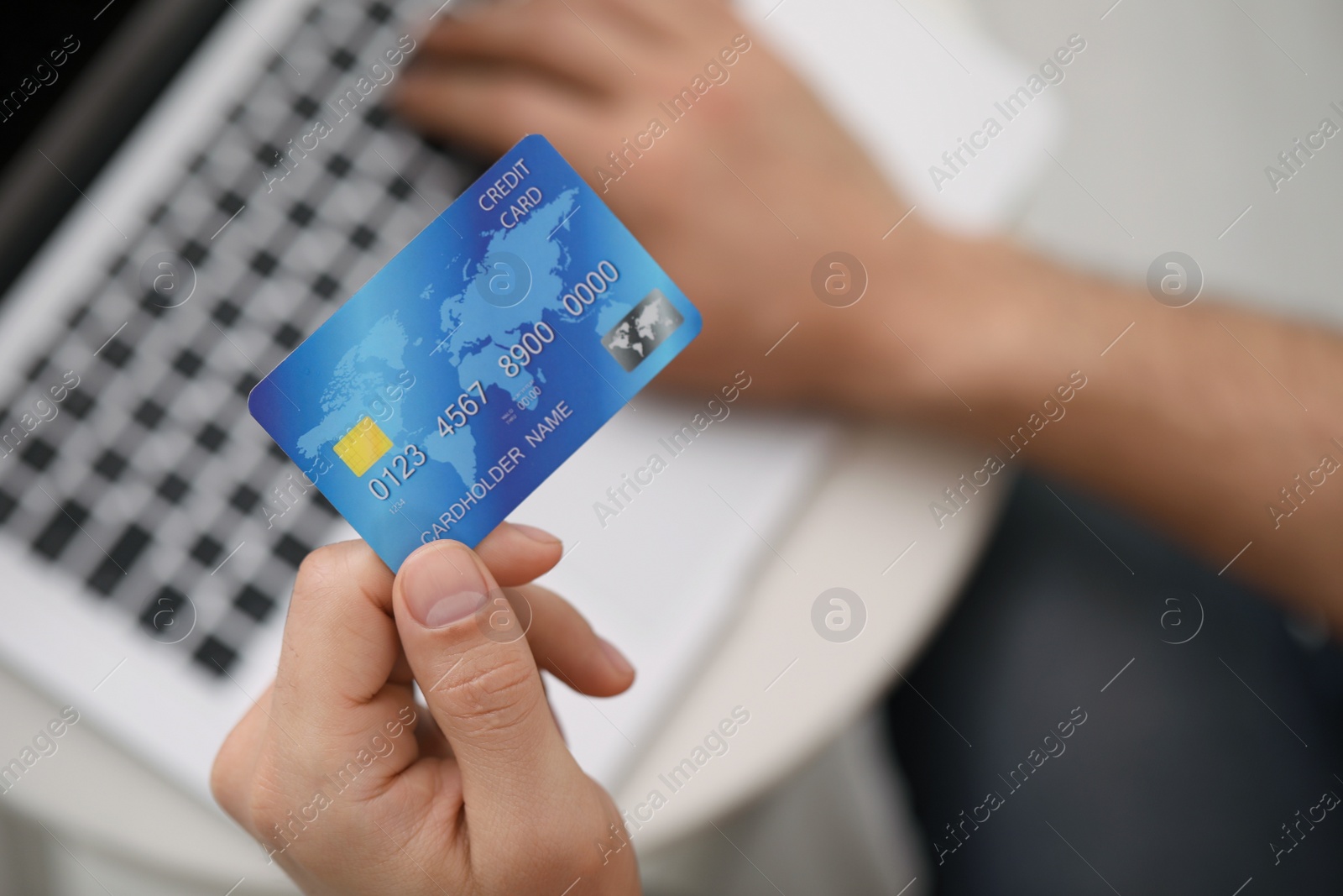 Photo of Man using laptop and credit card for online payment at table indoors, closeup