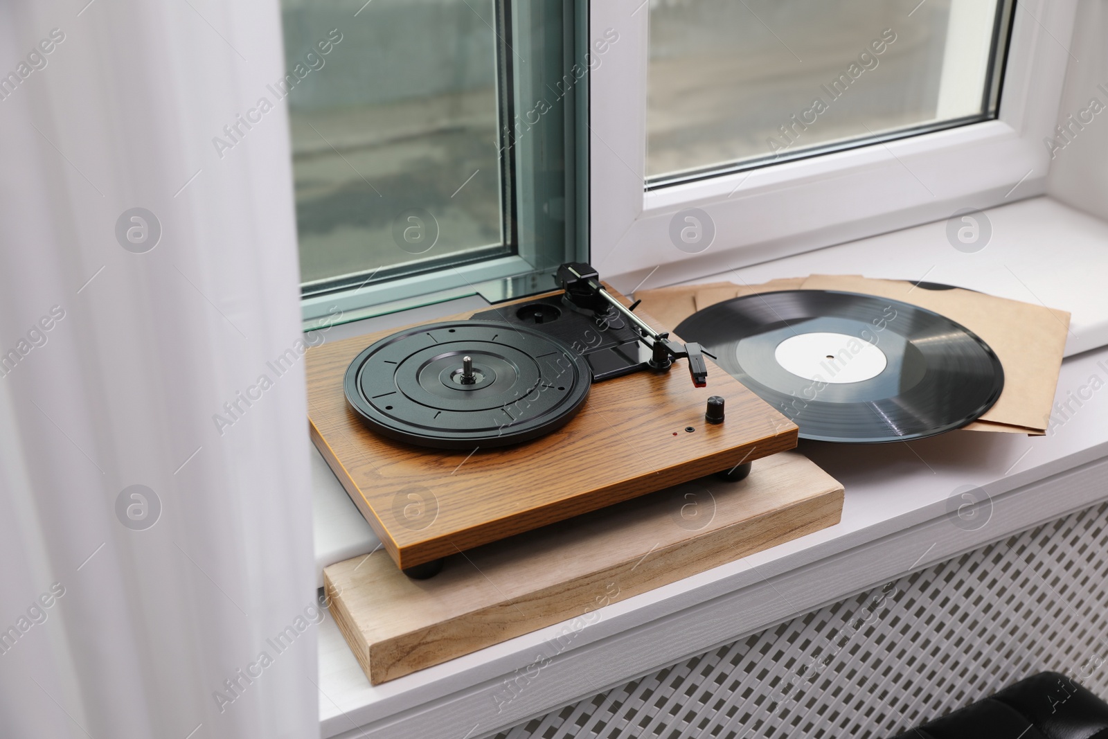 Photo of Stylish turntable with vinyl discs on windowsill in room
