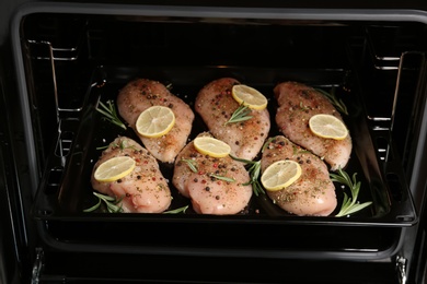 Photo of Chicken breasts with lemon and rosemary on baking sheet in oven