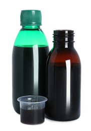 Bottles of cough syrup and measuring cup on white background