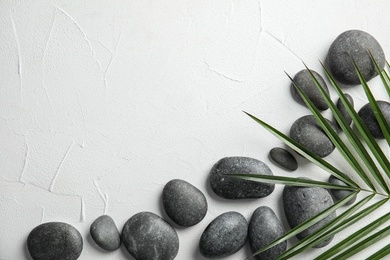 Zen stones and tropical leaf on light background, top view with space for text