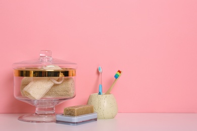 Photo of Composition of glass jar with luffa sponges on table near pink wall. Space for text