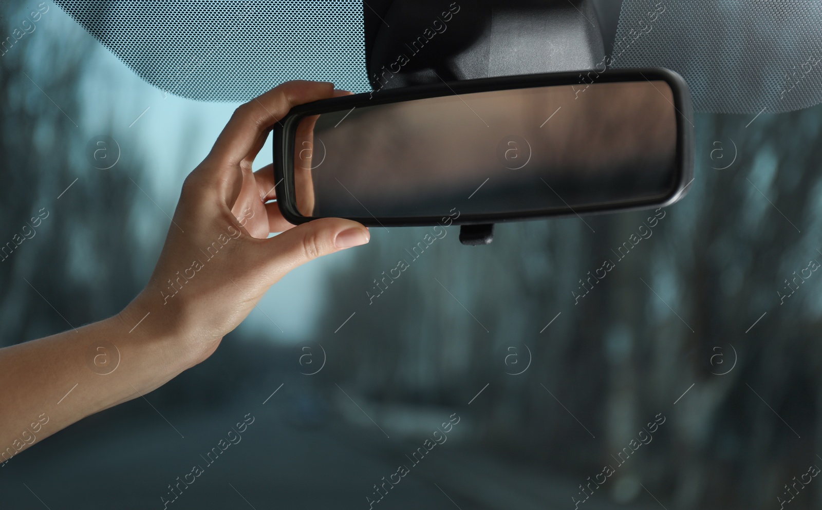 Photo of Young woman adjusting rear view mirror in car, closeup